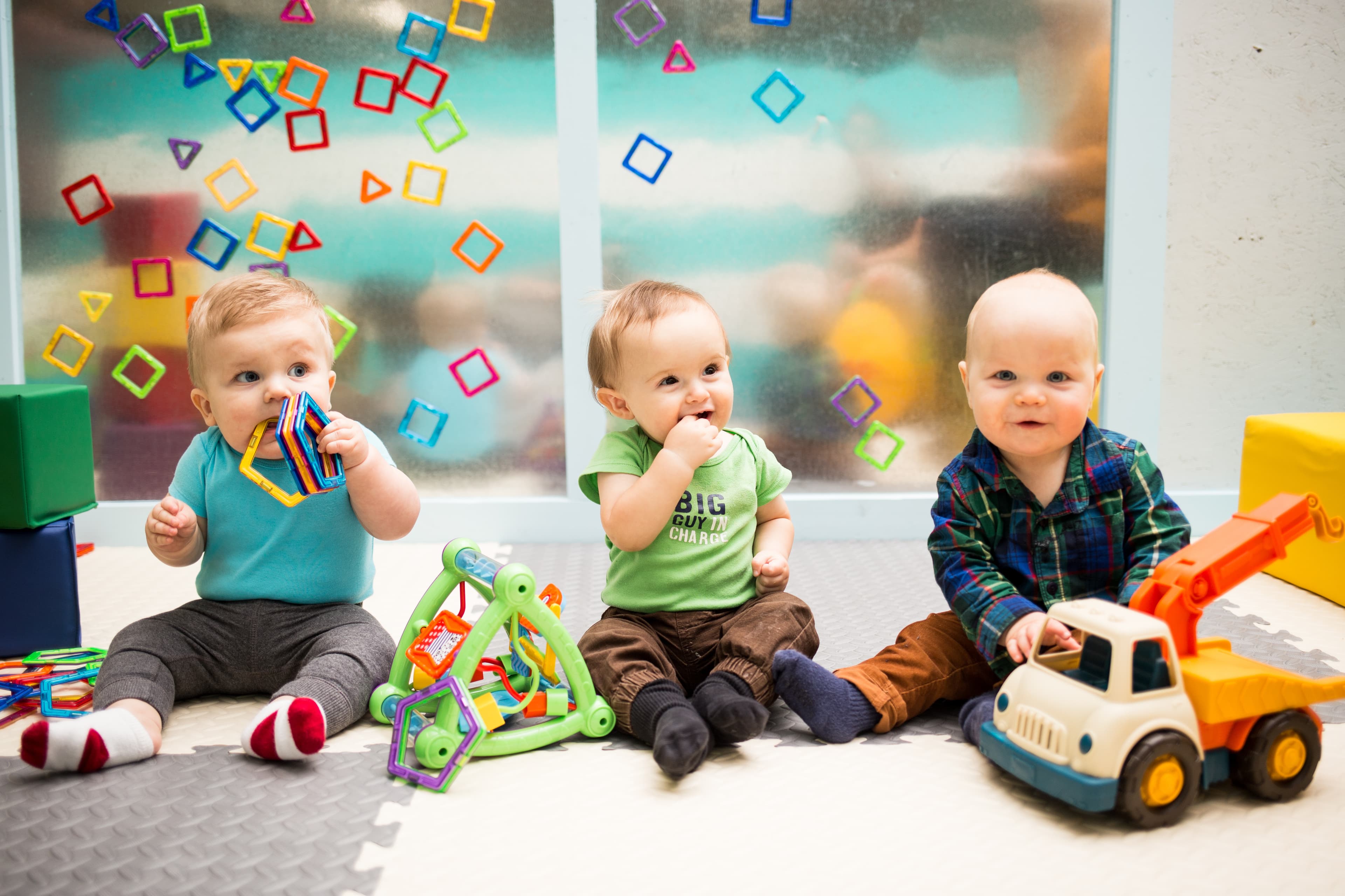 Three babies sitting together and exploring colorful play materials